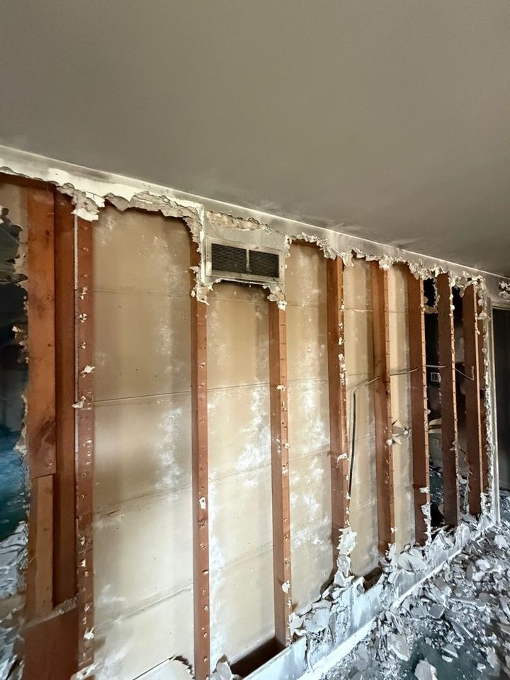 Wall with the damaged drywall cut away to bare studs, broken drywall pieces piled along the floor